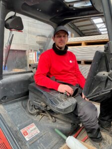 Werknemer van een doe-het-zelf zaak in rode trui in een werkvoertuig.